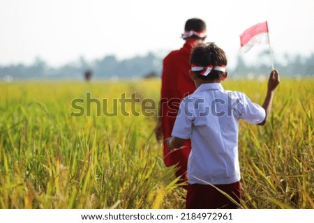 Asian school boy wearing uniform are walking together in the rice field while raising red white flag celebrating independence day.