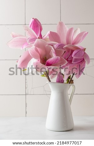Still life with pink magnolia flowers in vase on white tile background. Vertical orientation. Wedding or holiday concept
