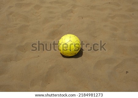 A picture of yellow ball on the sandy beach used for beach soccer.