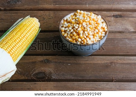 fresh sweet corn, dried corn in bowl on wooden table 