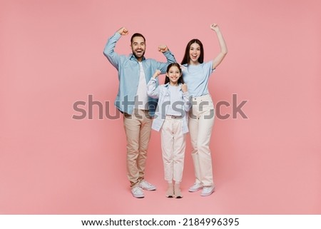 Full body young happy overjoyed parents mom dad with child kid daughter teen girl in blue clothes doing winner gesture celebrate clenching fists say yes isolated on plain pastel light pink background.