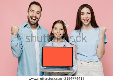 Young overjoyed parents mom dad with child kid daughter teen girl wear blue clothes use hold laptop pc computer blank screen workspace area do winner gesture isolated on plain light pink background.