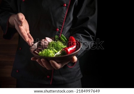 Plate with food in chef hand for presentation. Dark background free space for advertising.