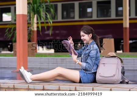 Asian tourist teenage girl at train station using smartphone map, social media check-in, or buy ticket booking. Modern travel app technology, lone traveler, Summer vacation railroad adventure concept