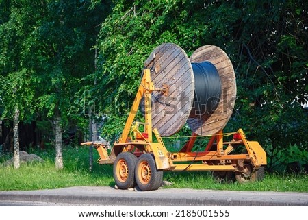 Wooden reel with fiber optic cable mounted on trailer for easy transportation. Laying optical fiber cable in suburb, fast internet concept. Cabling, laying of underground communications.  Royalty-Free Stock Photo #2185001555
