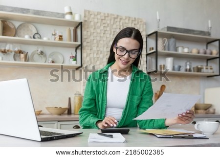 Smiling young beautiful woman reading banking paper notification about last mortgage payment while calculating budget at home. Happy millennial girl feeling excited of good news in letter notice. Royalty-Free Stock Photo #2185002385