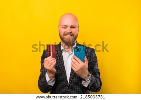 A picture of a businessman holding a credit card and his phone while smiling at the camera