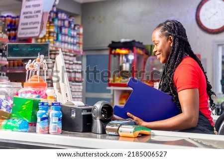 side view of a smiling African American cashier recording stocking using laptop holing clipboard