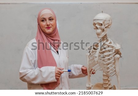 A Muslim female teacher teaches students using the human body skeleton model to explain anatomy in biology class in the classroom lab. Royalty-Free Stock Photo #2185007629