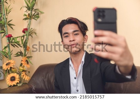 Photo of a young asian man taking a selfie. Creative portrait shot in preparation for posting on profile photo on social media.