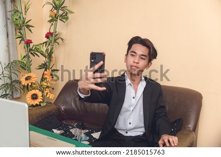 An industry professional taking a photo of himself. He is sitting on a sofa with a laptop before him.