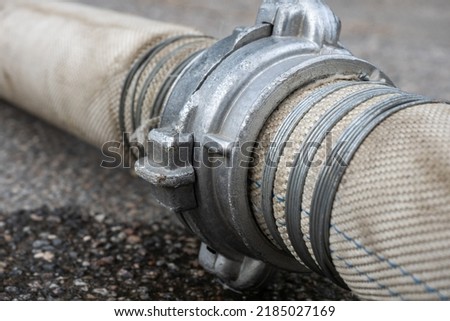 Fire service hose. Fire extinguishing equipment. Fabric hose with metal fitting. Fragment of hose with steel clamps. Fire hosepipe on asphalt close-up. Water flows out of hosepipe. Royalty-Free Stock Photo #2185027169