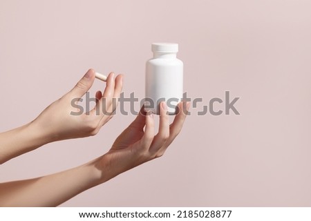 Woman holding pill and blank white plastic tube on pink background. Packaging for pill, capsule or supplement. Medic product branding mockup. High quality photo Royalty-Free Stock Photo #2185028877