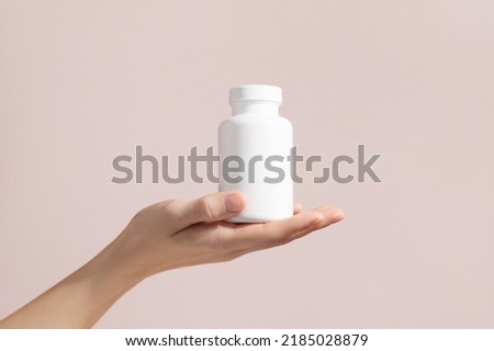 Young female hand holding blank white squeeze bottle plastic tube on pink background. Mockup. High quality photo Royalty-Free Stock Photo #2185028879