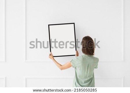 Woman holding blank picture frame against a wall. Artwork mockup concept