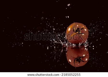 The tomato with drops stands on the black background