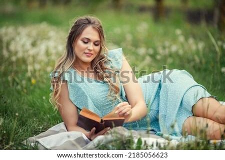 beautiful young woman in a romantic dress reads a second book in spring in a blooming garden