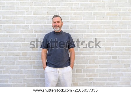 Trendy casual middle aged man posing in front of a brick wall in a relaxed stance with hands in his pockets Royalty-Free Stock Photo #2185059335