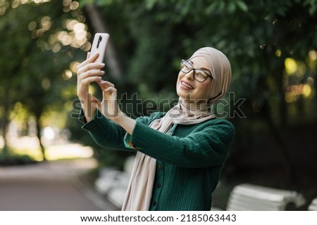 Portrait of smiling happy beautiful muslim woman relaxing using digital smartphone. Young muslim girl looking at screen speaking during online video call on social media on city.