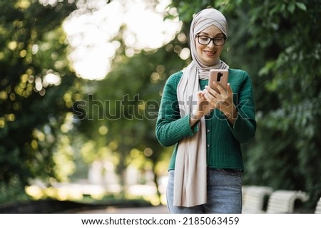 Portrait of beautiful smiling stylish muslim businesswoman with smart phone in hijab walking in summer park. Outdoor, park, business, gadget concept. Walking down the sunny city park.