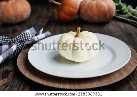 Holiday place setting with plate, napkin, and silverware on a Thanksgiving Day decorated table. White and Orange pumpkins. Selective focus with blurred foreground and background. 