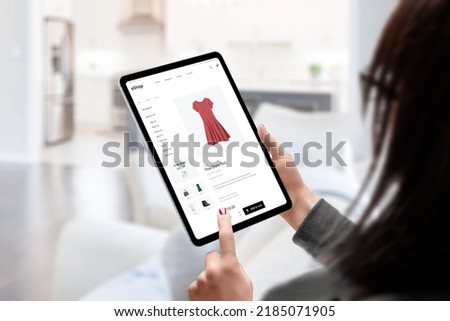Woman buys a dress online with tablet concept. Modern e-commerce clothing website. Living room in background Royalty-Free Stock Photo #2185071905