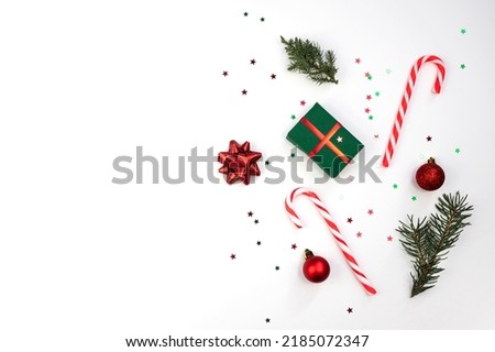 Christmas composition. Christmas gift, striped caramel, red balls, fir branches on a white background. Flat lay, top view, copy space.
