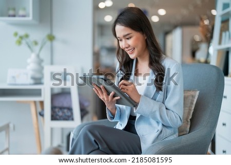 smart casual asian female startup entrepreneur small business owner business woman smile hand use tablet working organize inventory products shelf checking in showroom studio office daytime background Royalty-Free Stock Photo #2185081595