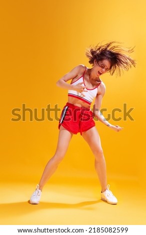 Portrait of emotive young woman in top and red shorts posing isolated over yellow background. Playing an imaginary guitar. Concept of beauty, style, emotions, fashion, lifestyle, facial expression, ad