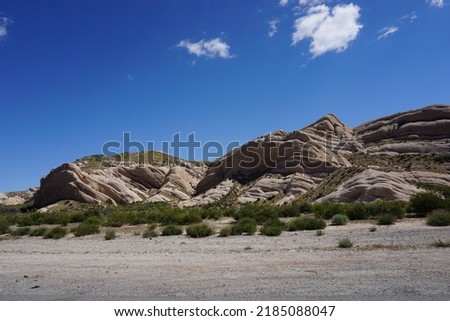 Beautiful landscape showing rose color sandstone rocks in the background with the blue summer sky above and beige desert land with tiny green shrubs in the foreground in Cajon Pass, Phelan, California