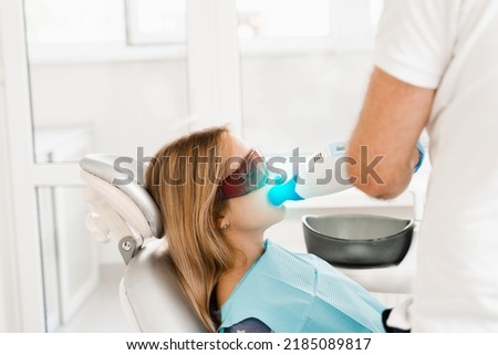 Artificial teeth whitening. Dental ultraviolet whitening treatment with light, fluoride and laser. Woman in red protective glasses patient do UV teeth whitening procedure Royalty-Free Stock Photo #2185089817