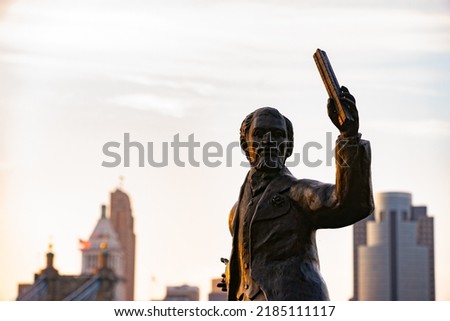 John A. Roebling statue with Cincinnati skyline in the background. John holding long metal object during magic hour.
