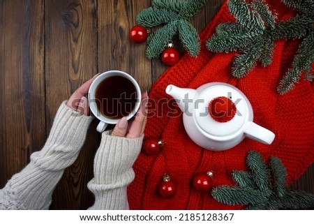 Tea is poured in a white teapot and glass, next to it lies a red plaid, Christmas balls and coniferous branches