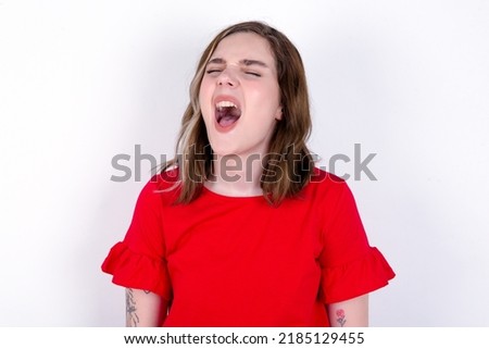 young caucasian woman wearing red T-shirt over white background angry and mad screaming frustrated and furious, shouting with anger. Rage and aggressive concept.