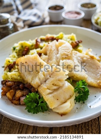 Fish dish - fried cod fillet with potato puree and bacon on wooden table 
