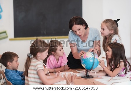 Female teacher with kids in geography class looking at globe. Side view of group of diverse happy school kids with globe in classroom at school. Royalty-Free Stock Photo #2185147953