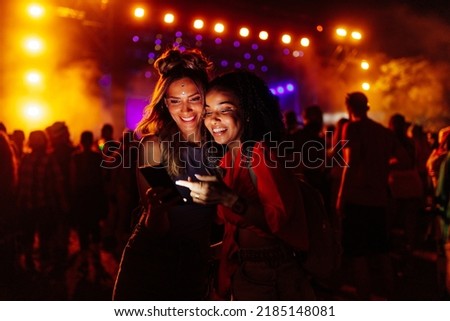 Two biracial women in a crowd at a concert using cellphone together Royalty-Free Stock Photo #2185148081