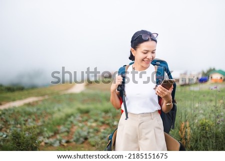 Tourist backpacker woman with backpack using smartphone on village and fog background. Young female traveler searching internet during vacation trips. booking and planning for a trip.