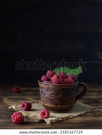 Large ripe raspberries in a clay cup on a canvas napkin. Dark brown wooden background