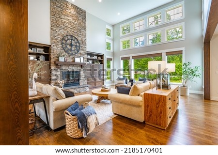 Large living room with exposed beam ceiling stone fireplace expansive windows hardwood flooring and built in shelving Royalty-Free Stock Photo #2185170401