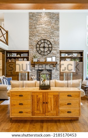 Large living room with exposed beam ceiling stone fireplace expansive windows hardwood flooring and built in shelving Royalty-Free Stock Photo #2185170453