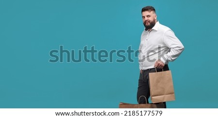A Caucasian-looking man with a brown paper bag on a blue background. A man with a white shirt with shopping bags. Studio shot of a man with purchases. Space for text.