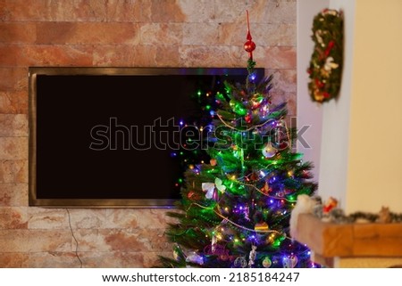 A green Christmas tree with Christmas decorations stands in the room. A large plasma TV hangs on the wall at the back.



