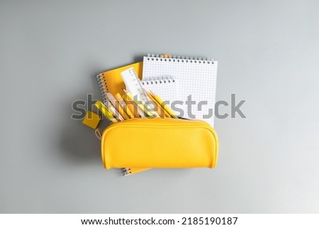 Back to school concept. Yellow school pencil case with filling school stationery, notebook, pens, pencils. Yellow school accessories on grey background. Flat lay, top view, copy space Royalty-Free Stock Photo #2185190187