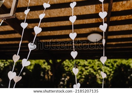 Lots of white paper homemade hearts hanging from a ribbon outdoors. Photography, decoration.
