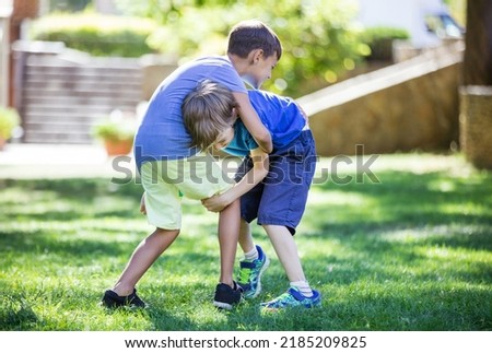 Two boys fighting outdoors. Siblings or friends wrestling on grass in summer park. Siblings rivalry.