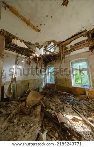 Sunlit grungy room with hole in wooden ceiling and garbage on floor inside desolate building Royalty-Free Stock Photo #2185243771