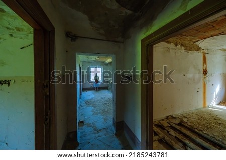 Female standing near window in grungy hallway with weathered floor inside desolate building in daytime Royalty-Free Stock Photo #2185243781