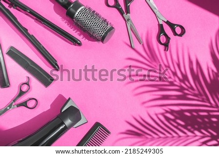 Scissors, combs, hair dryer and hair straightener lie on the left in a semicircle on a lilac background with copy space and a shadow of a palm tree on the right, flat close-up. The concept  hairdresse