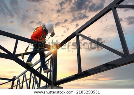 A Welders on risk areas. Steel roof truss welders with safety devices to prevent falls from a height in the construction site. Royalty-Free Stock Photo #2185250531